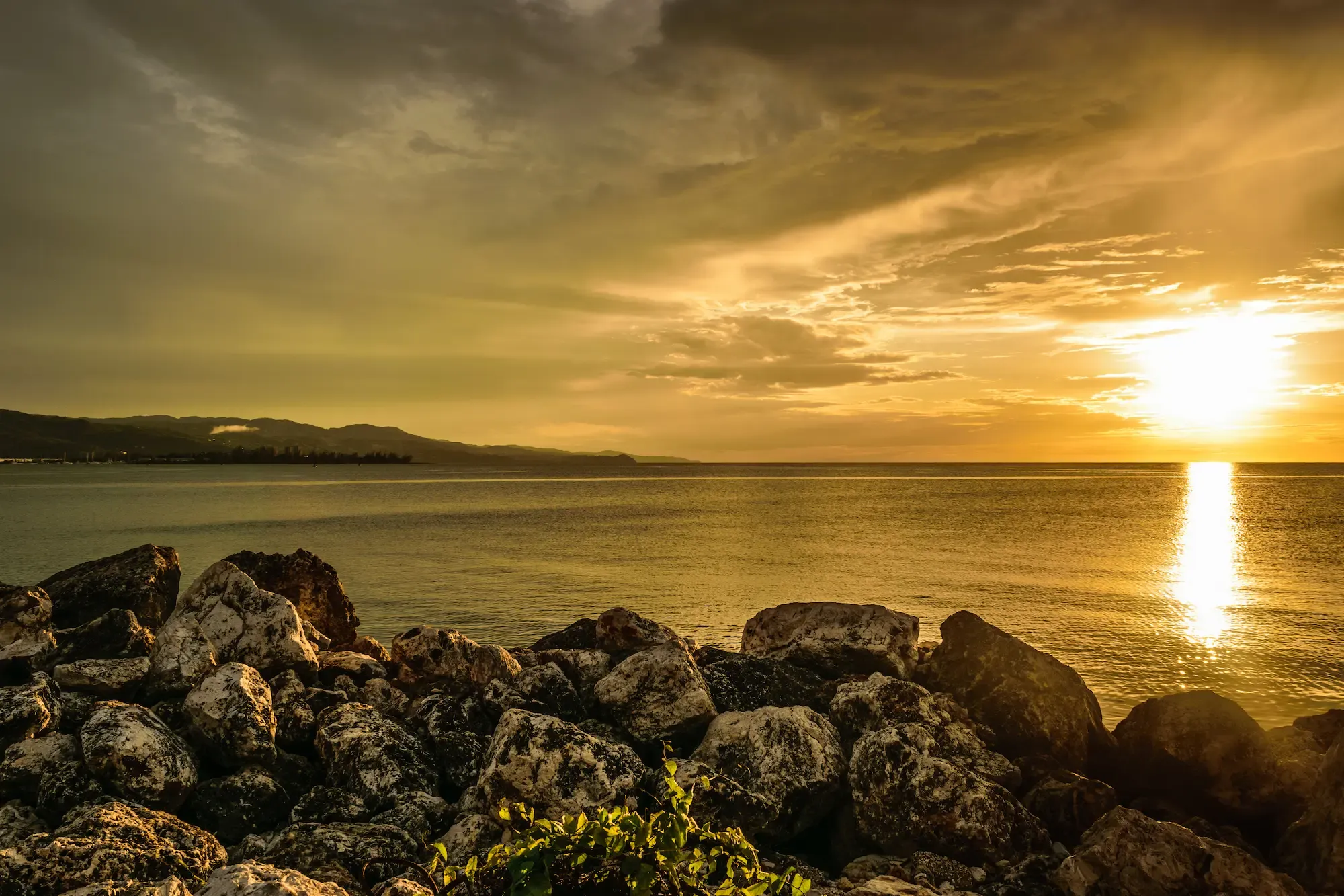 Golden sunset across Montego Bay with rocks along the shoreline
